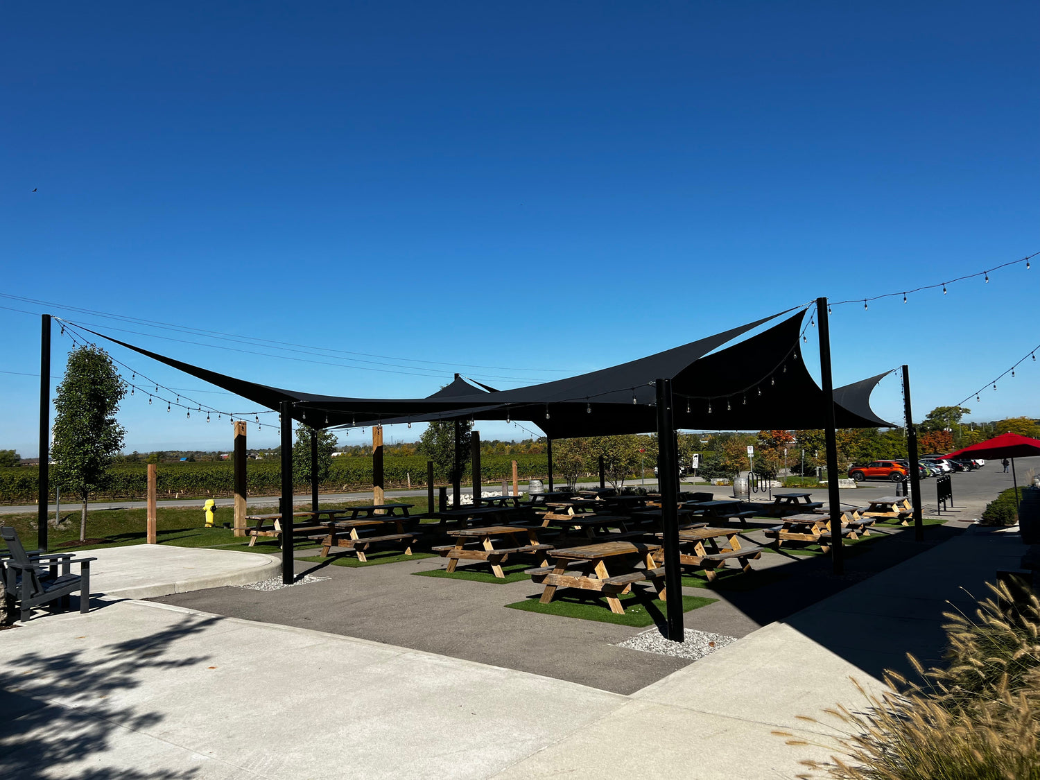 black shade sail over a patio with picnic tables on a sunny day showcasing the stunning landscape design