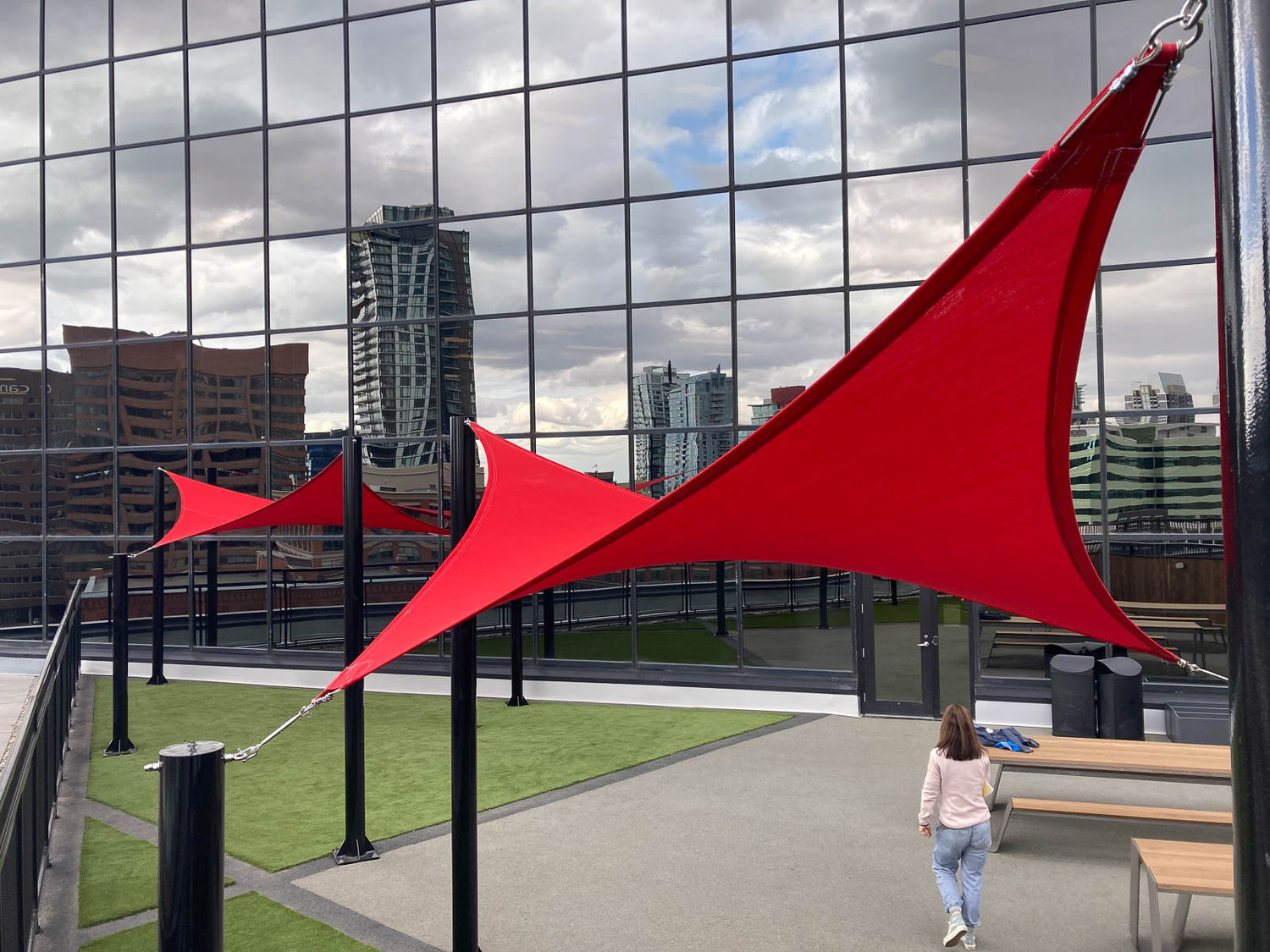 Urban rooftop setting maximizing usable space with tensile shade structures using vibrant red sails for shaded seating and walkway zones.