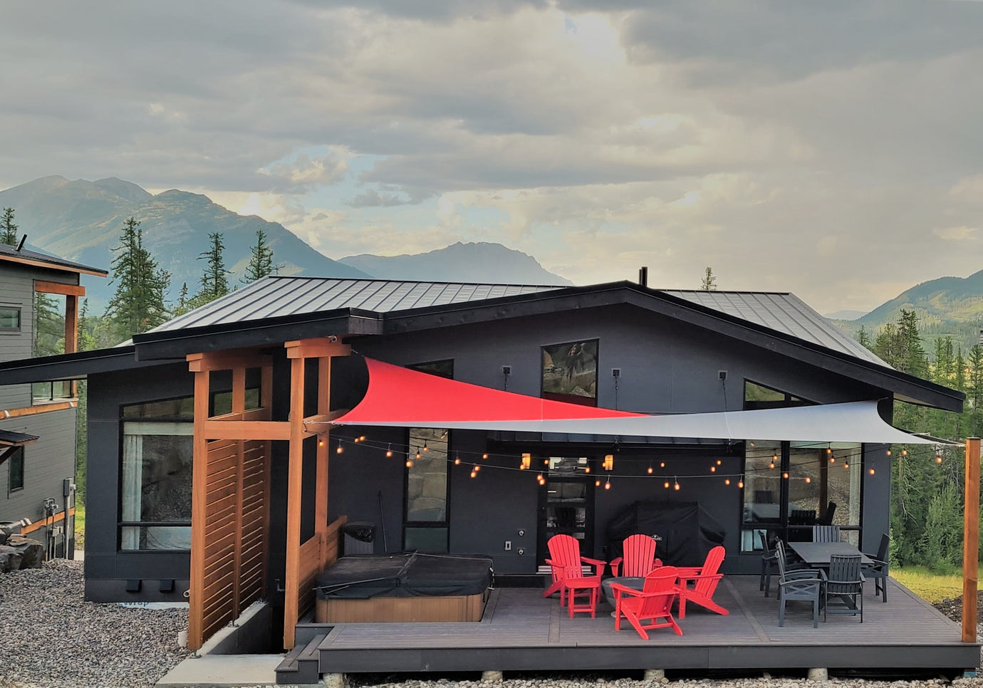 Image of a modern grey house nestled amidst mountains, featuring a backyard deck adorned with a patio set and a red and grey backyard canopy, offering a picturesque view of the surrounding landscape.
