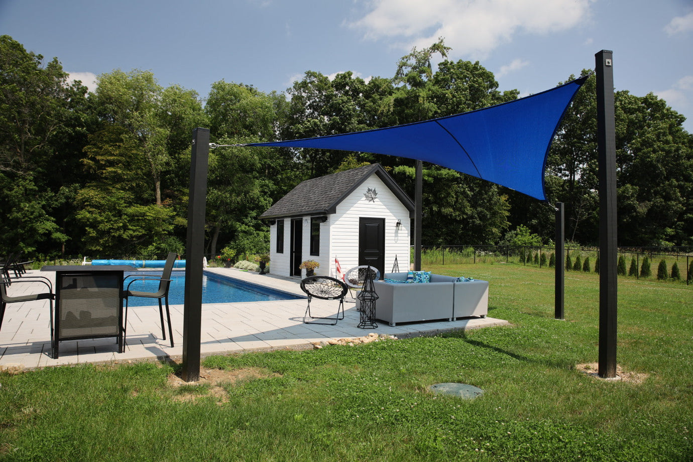 relaxing pool area surrounded with greenery and a blue shade sail for sun protection showcasing commercial patio design
