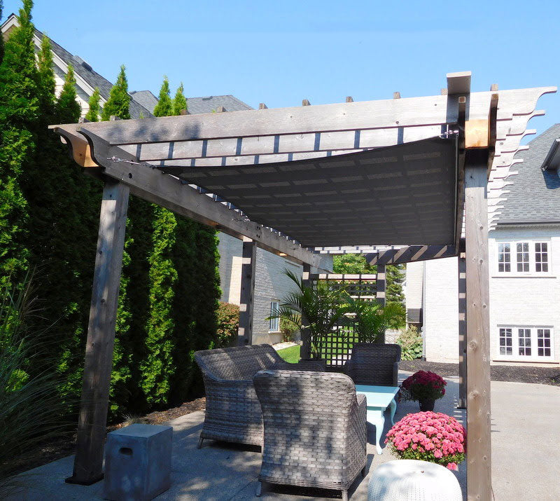 Modern residential landscape design featuring a shaded pergola with outdoor seating and lush greenery.