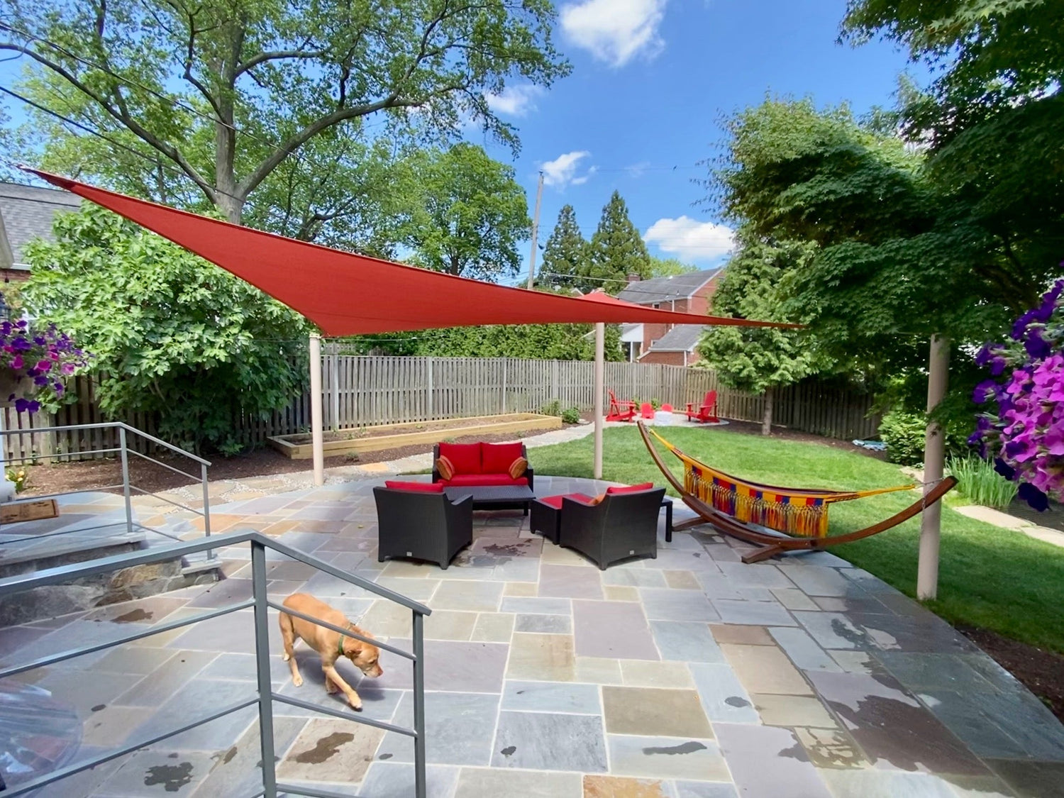 Backyard patio with red shade sail, outdoor seating, and hammock, showcasing versatile outdoor setups often built alongside equipment shed kits.