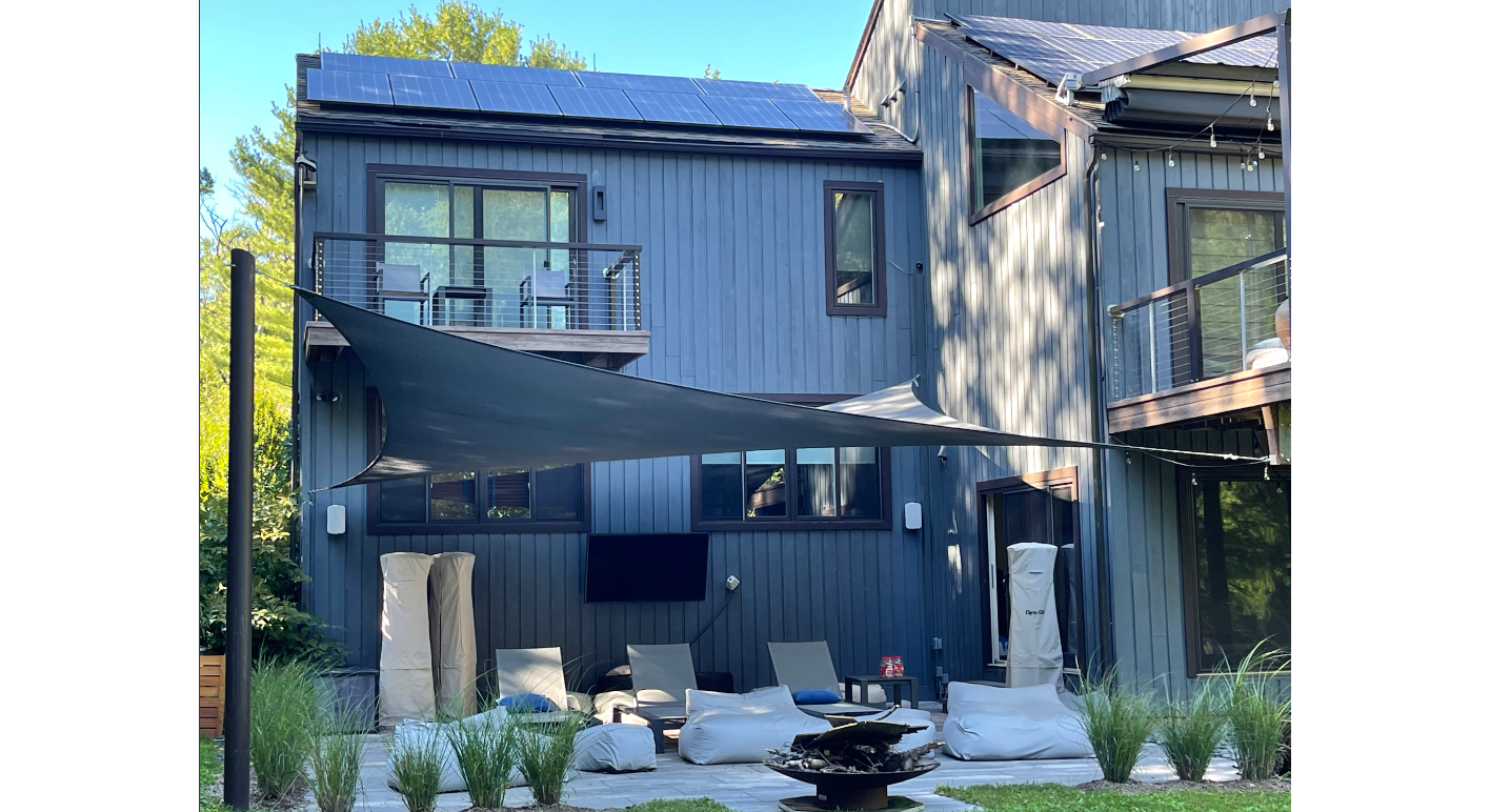 image of the backyard of a modern house with a shade sail over the patio providing sun shade solutions.