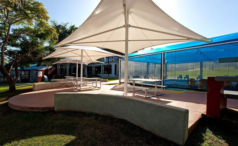 Outdoor seating area with large white shade umbrellas supported by sturdy umbrella stand bases surrounding picnic tables.