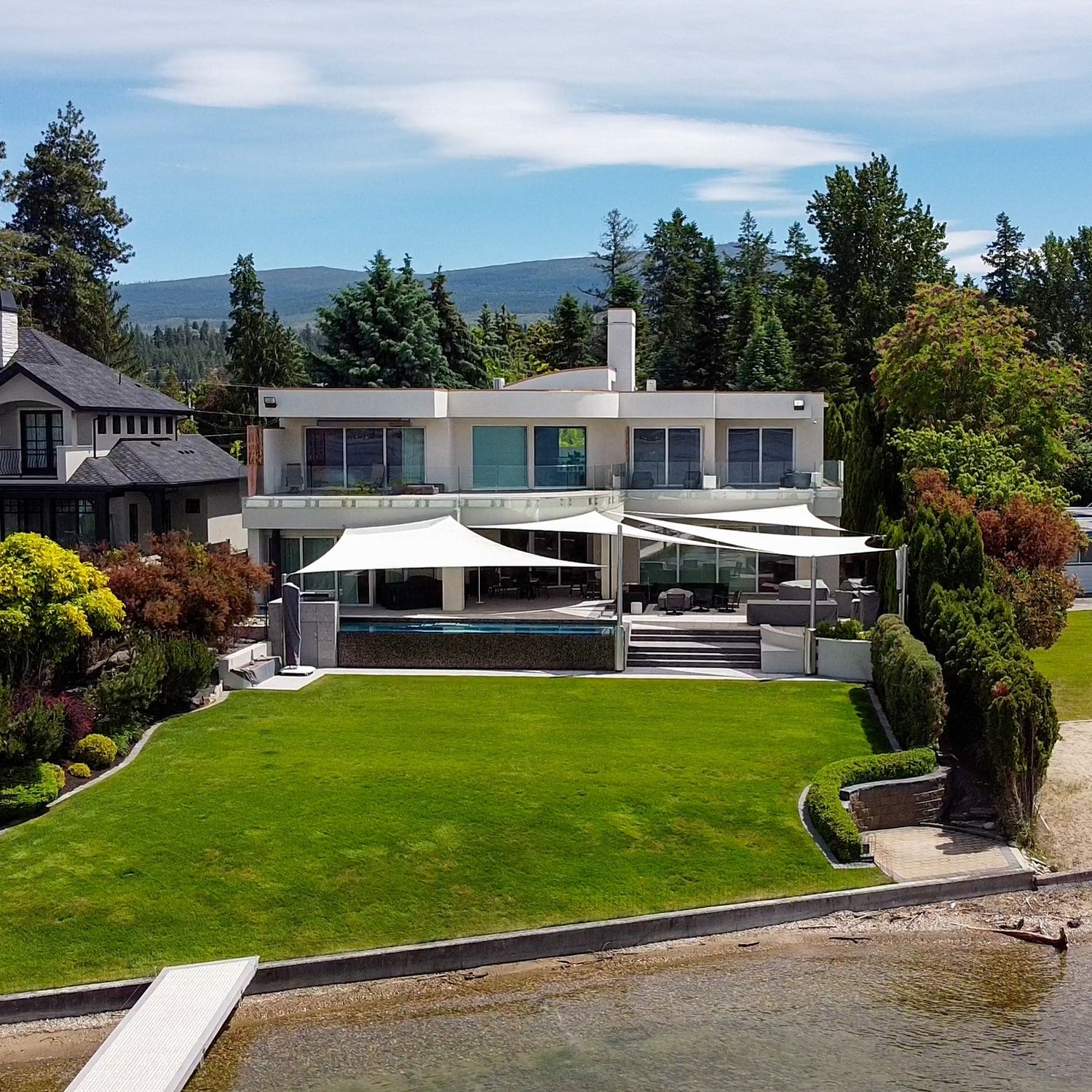 Modern waterfront home featuring large white tensile canopies, showcasing innovative shade design for patio and poolside comfort.