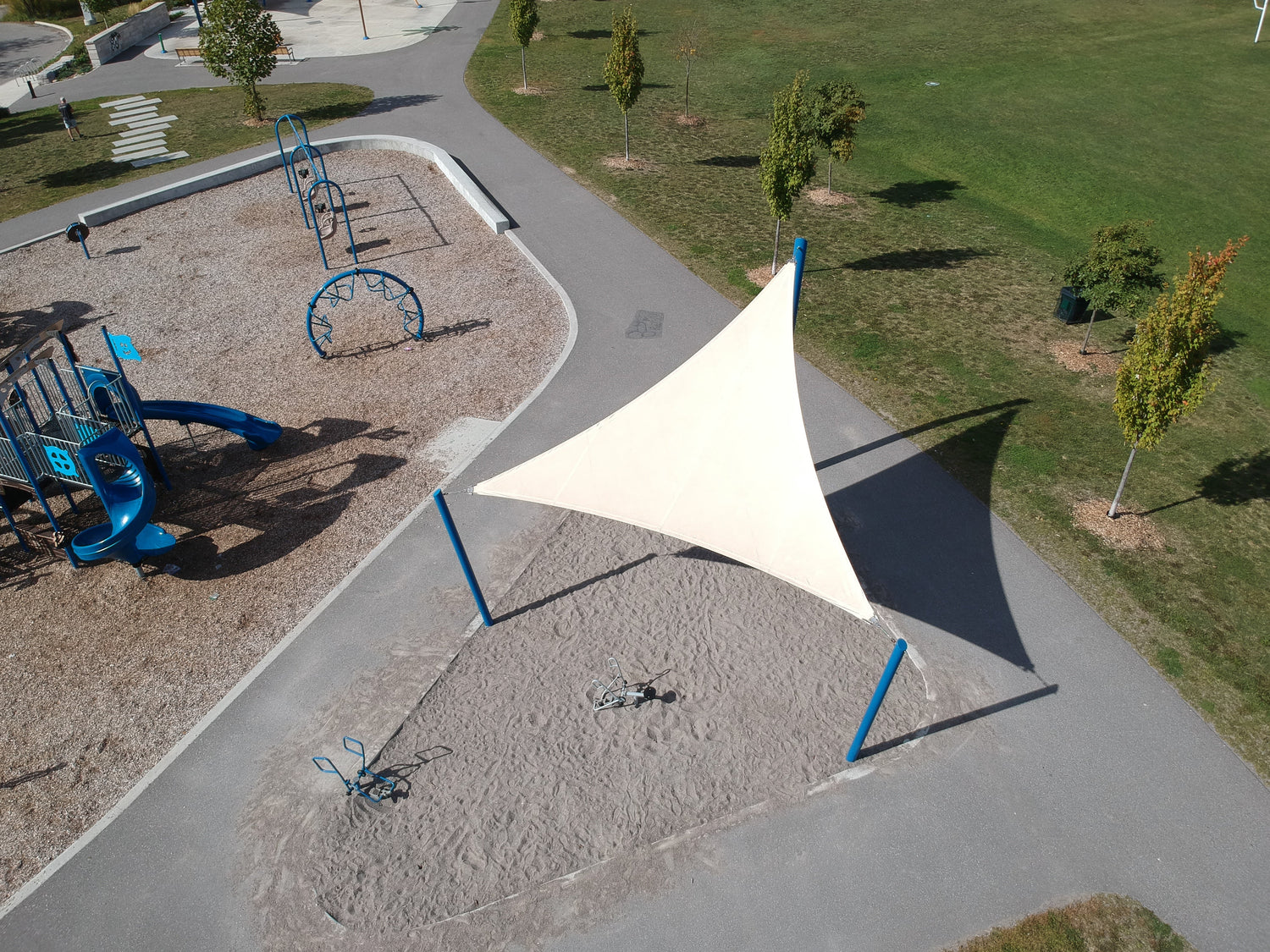 Playground featuring a triangular shade sail made from fabric with a strong UV rating, offering reliable sun protection for children and families.