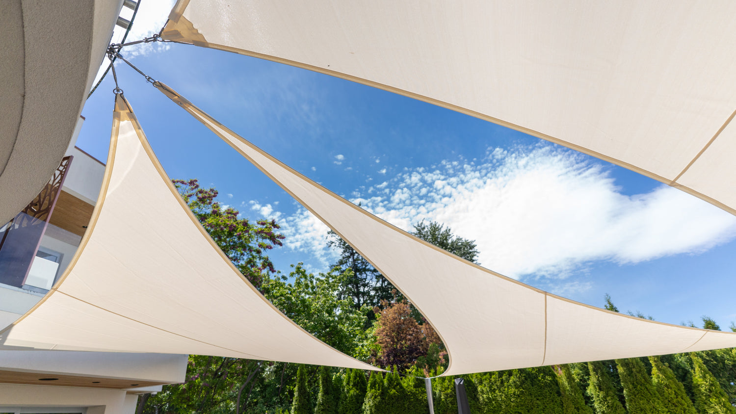 Outdoor personalized shade canopy installation featuring overlapping beige sail panels creating stylish sun protection against a bright blue sky.