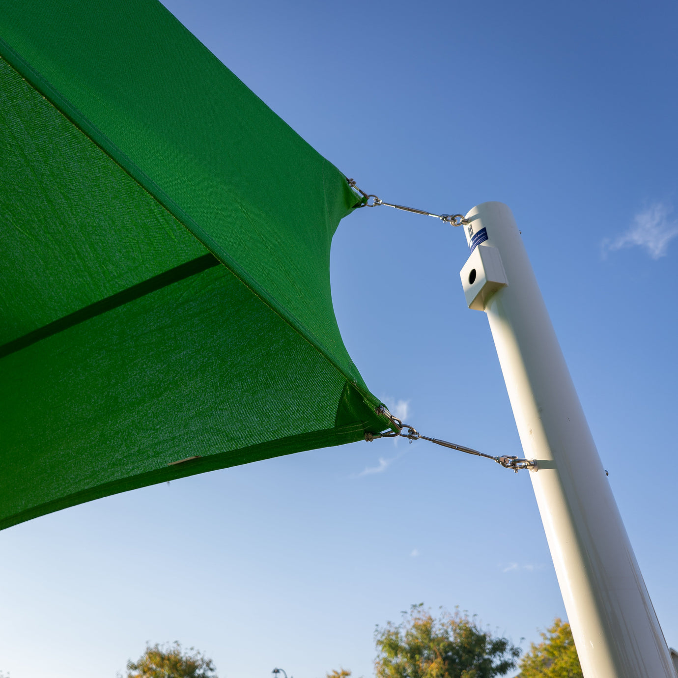 A close-up view of a green water resistant shade sail securely attached to a metal post, demonstrating strong outdoor weather protection.