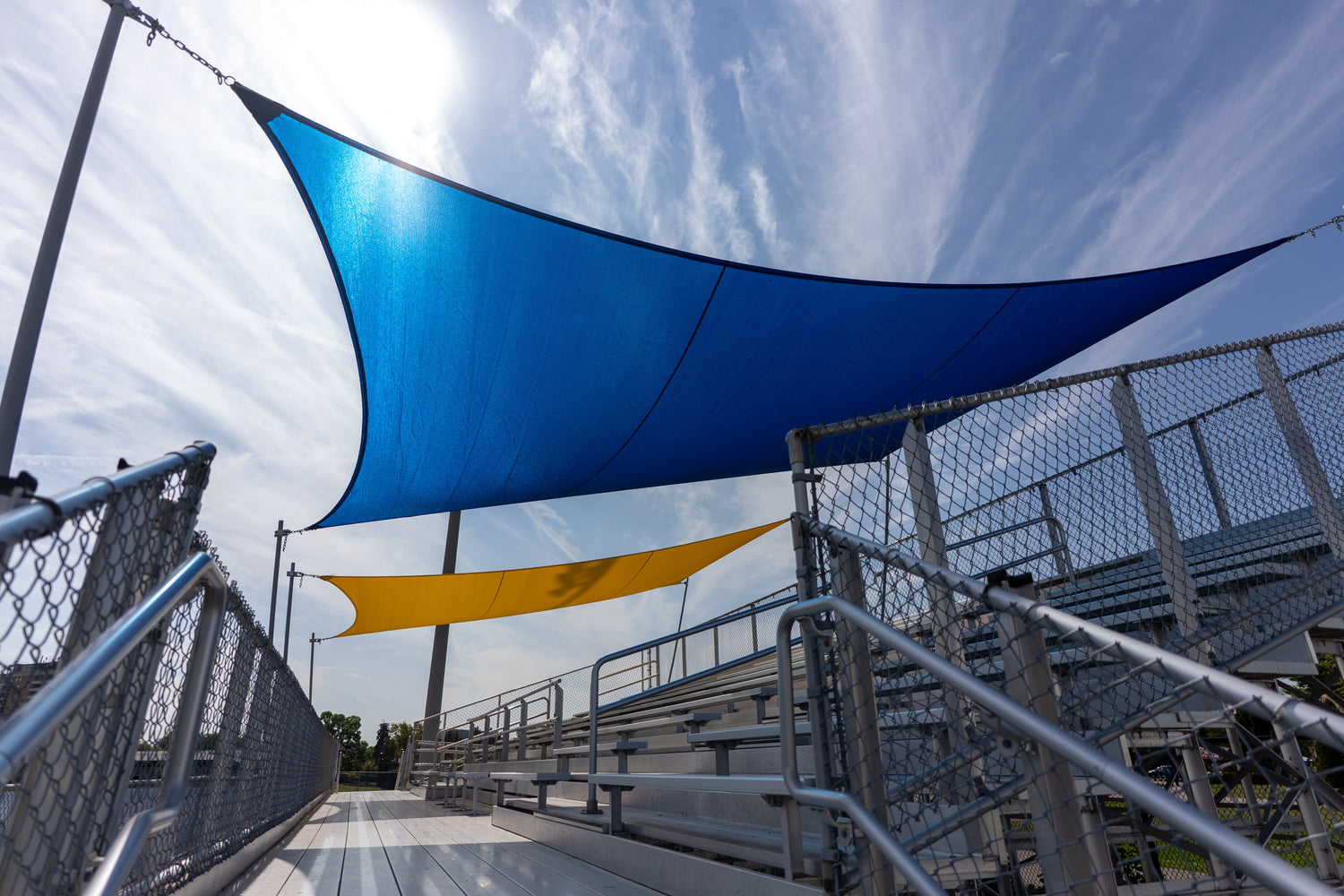 Outdoor bleacher seating covered by a blue and yellow Heavy Duty Shade Sail providing strong UV protection and durable weather-resistant shading.