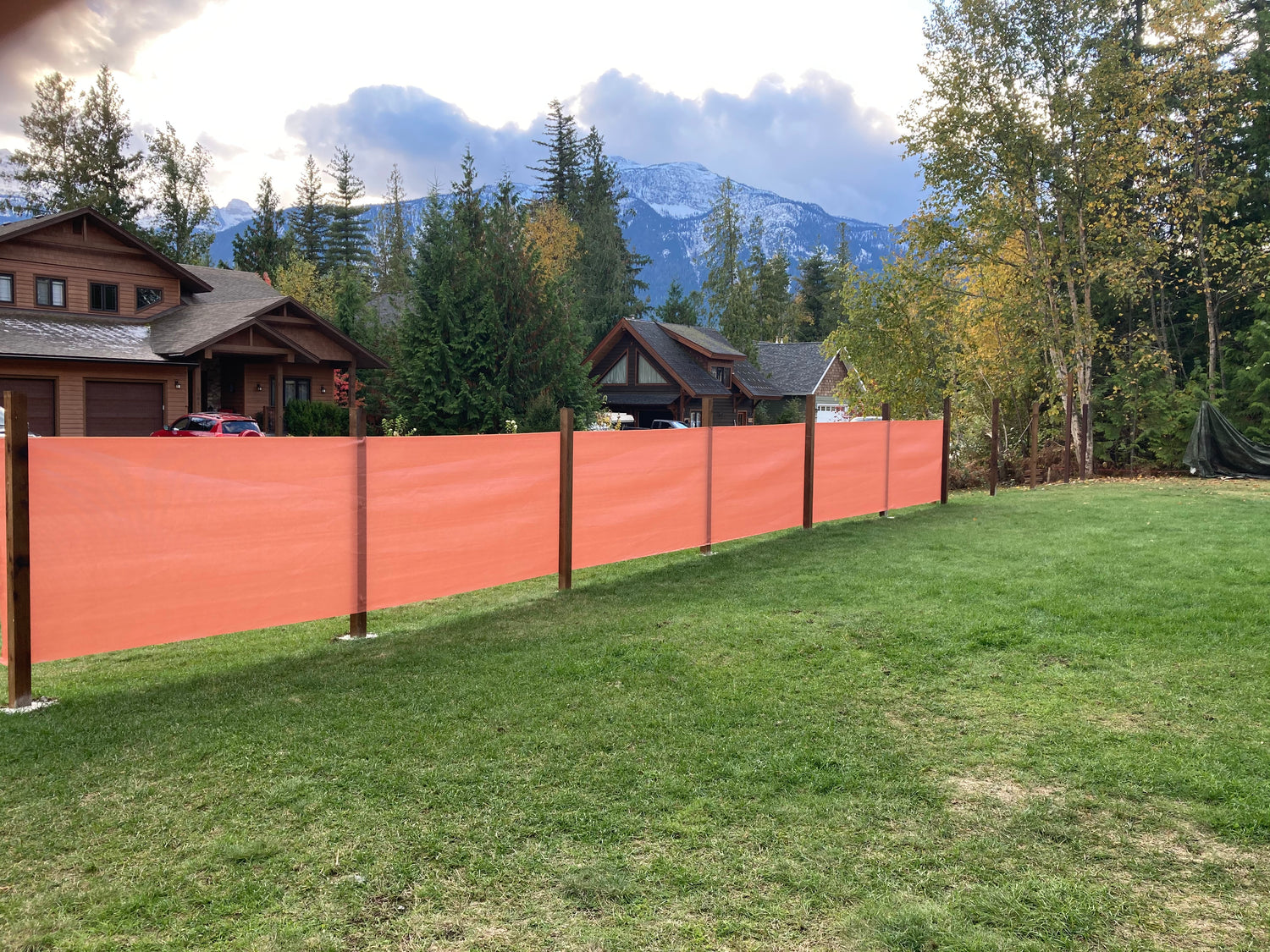 A scenic backyard view featuring a long orange sailcloth shade attached to wooden posts, providing a stylish and effective barrier for privacy and wind protection in a mountainous residential area.