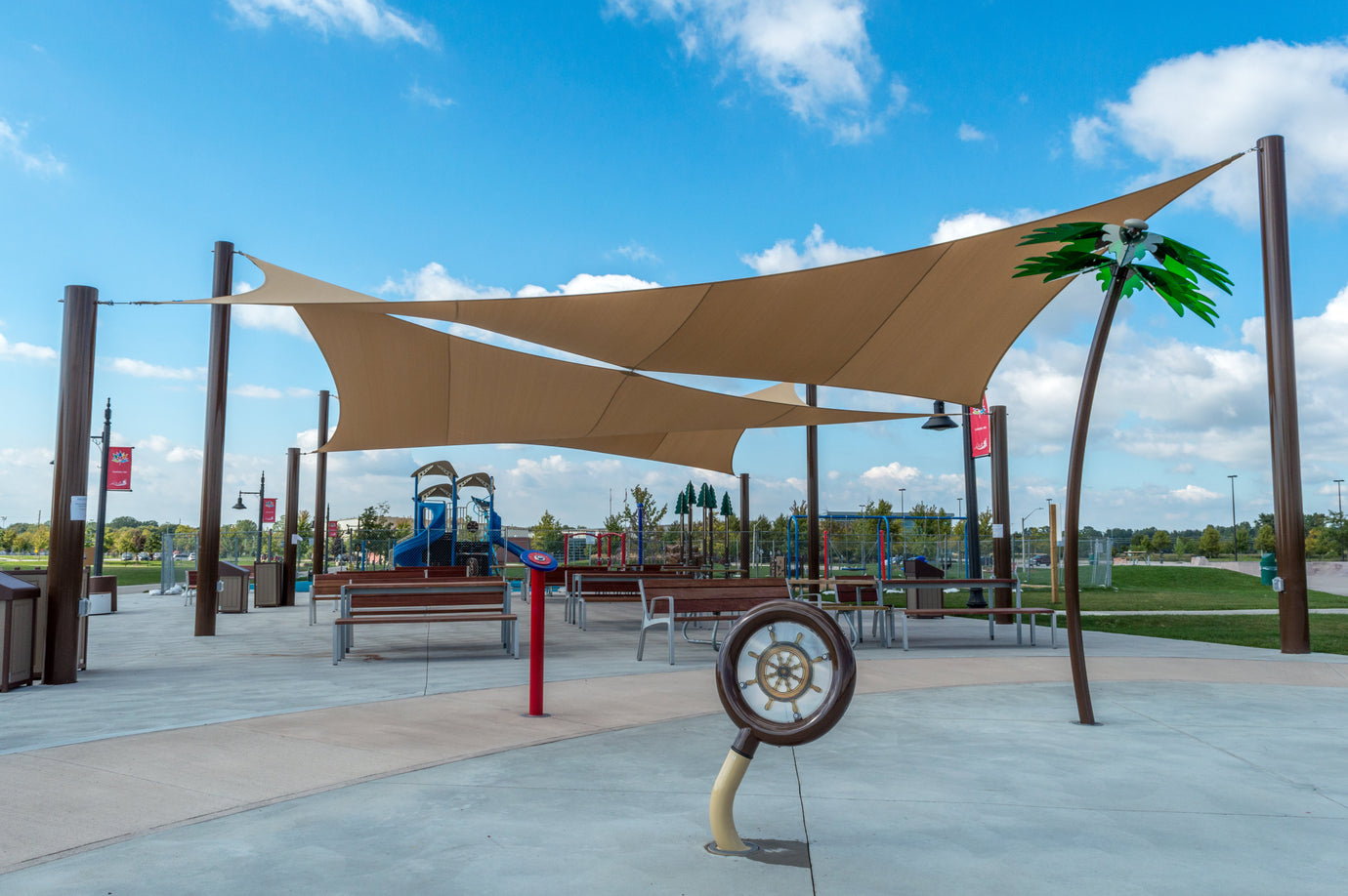 A modern outdoor area with large shade sails covering benches and play structures, showcasing commercial playgrounds designed for comfort and sun protection.