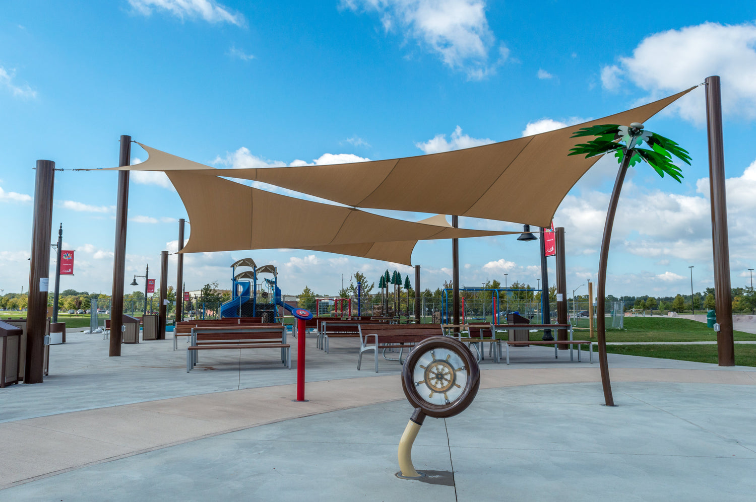 A modern outdoor area with large shade sails covering benches and play structures, showcasing commercial playgrounds designed for comfort and sun protection.