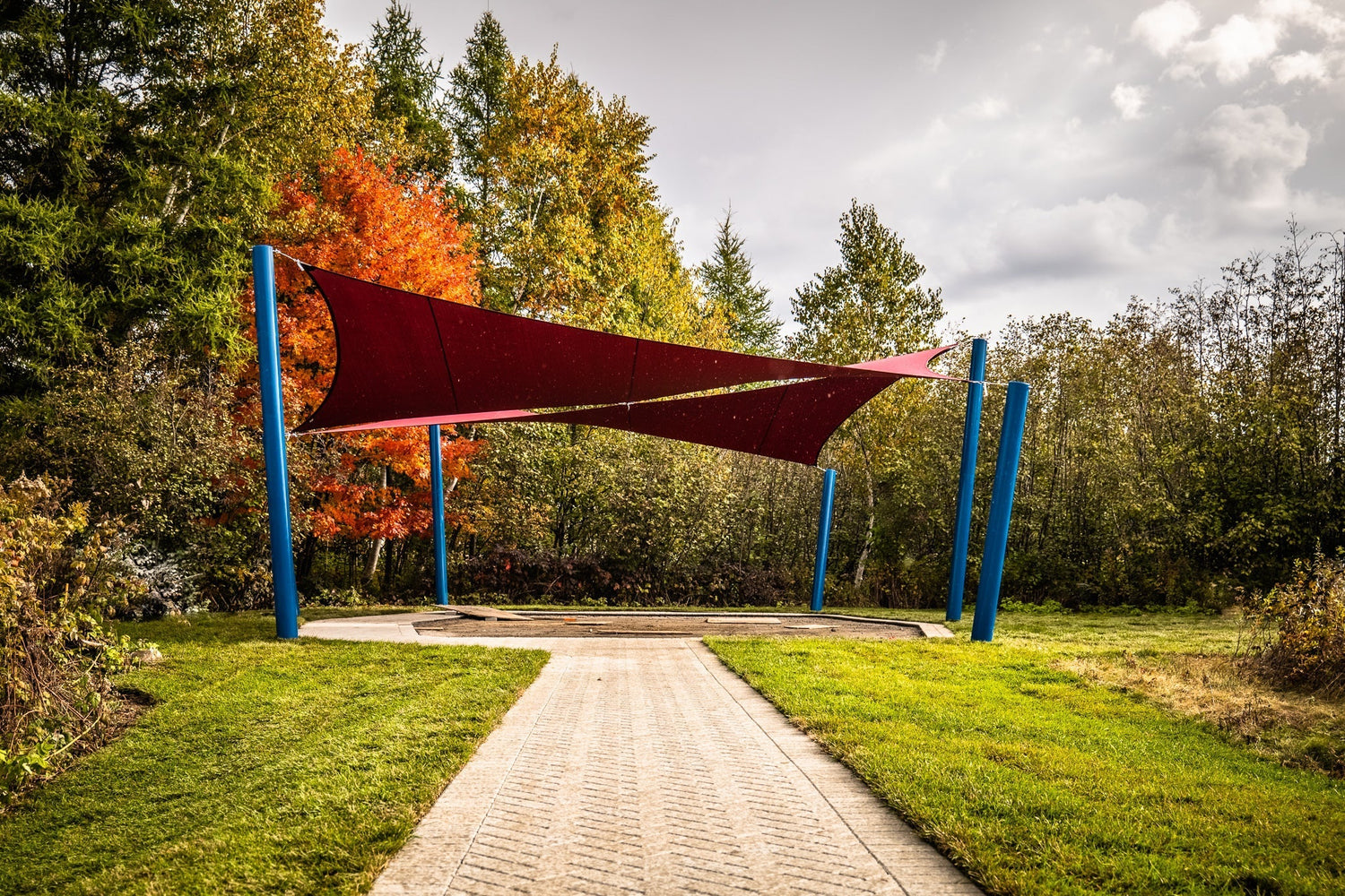 Red shade sails tensioned between vibrant blue shade sail posts in a landscaped outdoor area during fall, showcasing secure installation and seasonal durability.