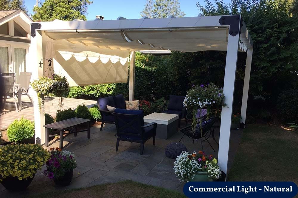 beige retractable shade canada over a backyard patio with chairs and greenery.
