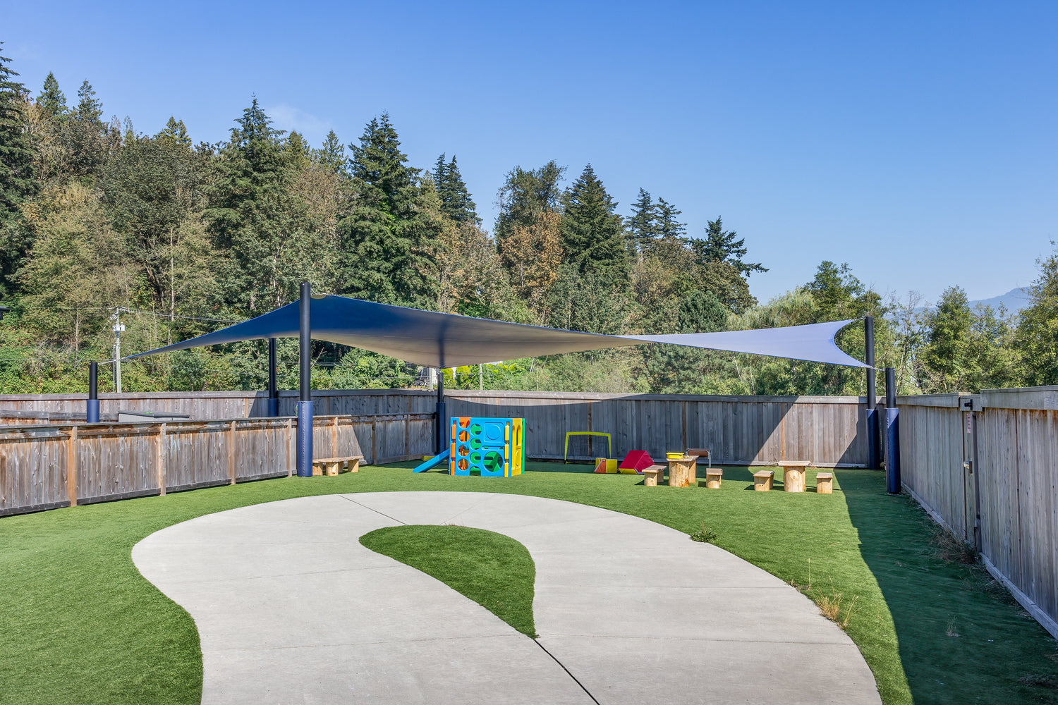 Outdoor play space featuring modern playground hardware with integrated shade sails, soft surfacing, and interactive play elements.