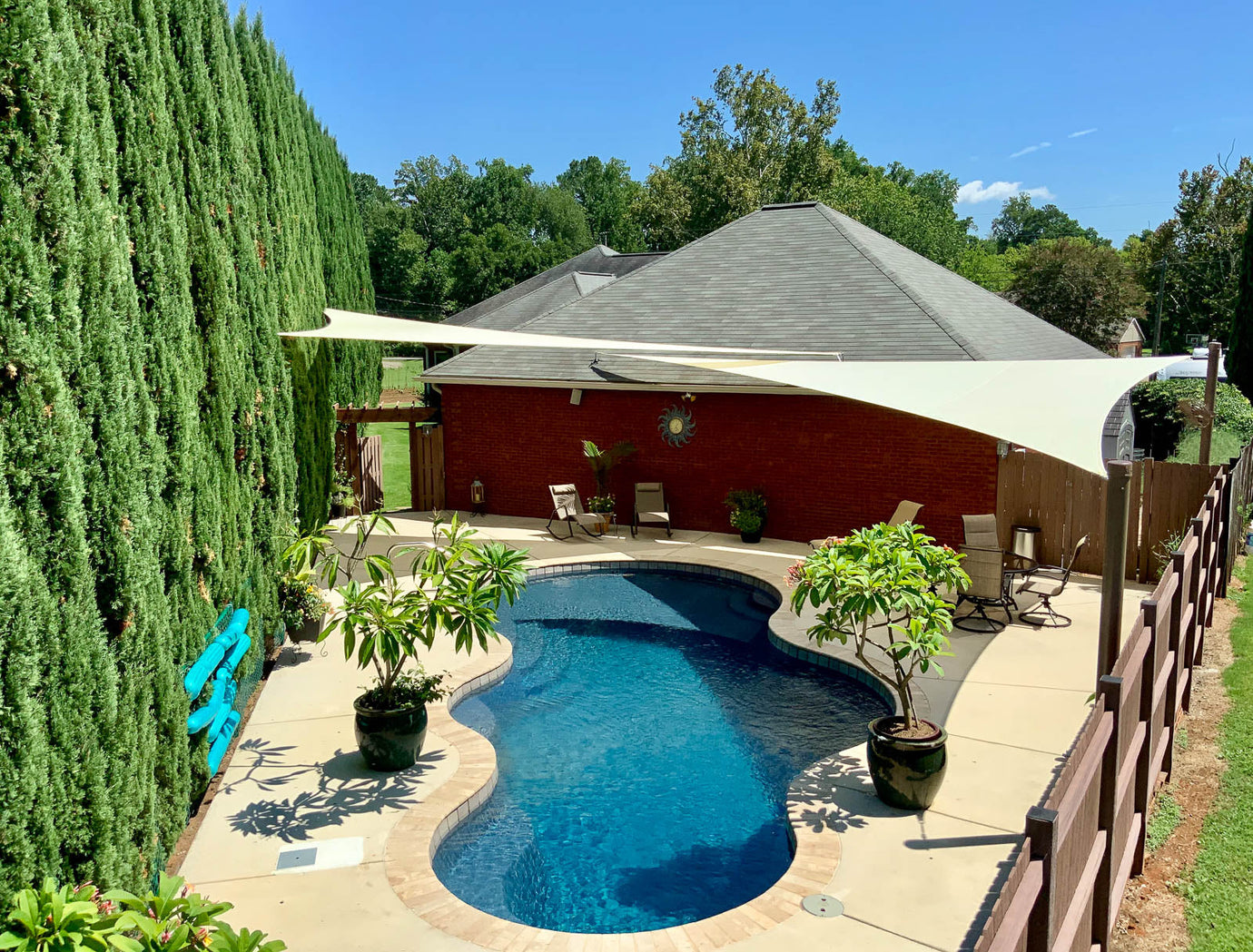 Cream sail canopy spanning a backyard pool, providing broad garden cloth shade for swimmers and poolside seating.