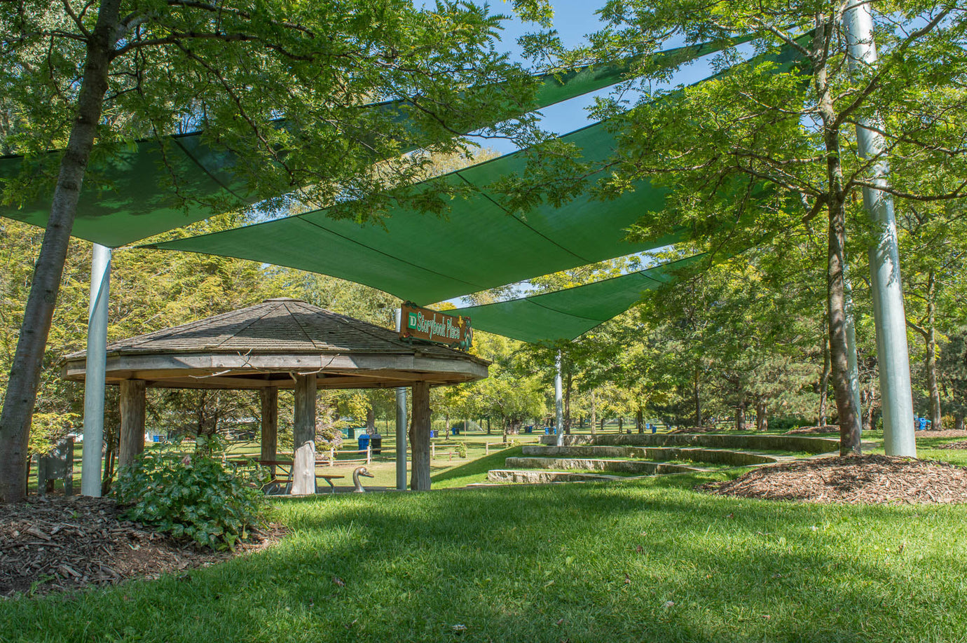 Green sun shade sail canopy providing shaded outdoor seating in a park area, demonstrating essential maintenance tips for sun shade sail canopy longevity and performance.