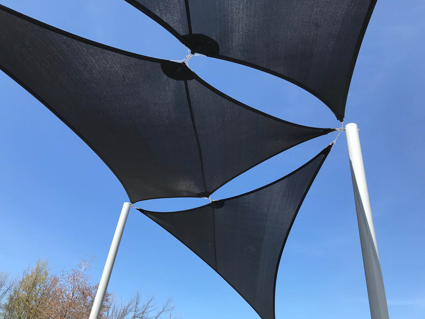 Triangular black shade sails tensioning tightly between white steel posts against a clear blue sky, showing proper shade sails tensioning for a modern outdoor structure.