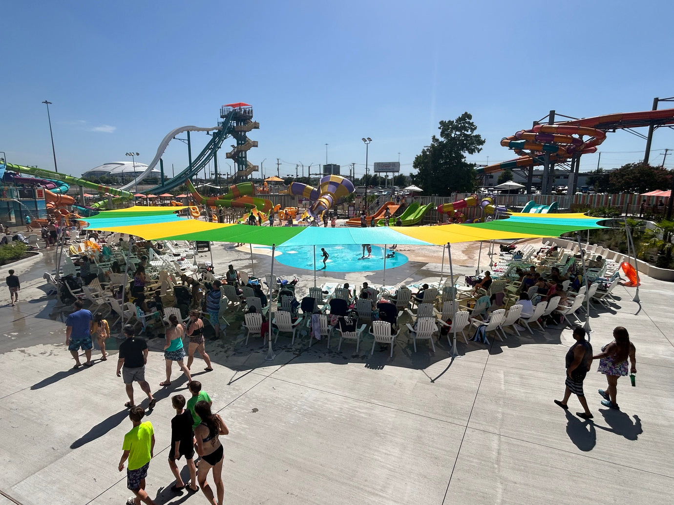 Colorful HDPE shade fabric sails providing UV protection over seating areas at a busy waterpark on a sunny day.