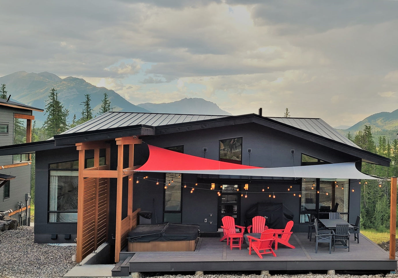 Image of a modern grey house nestled amidst mountains, featuring a backyard deck adorned with a patio set and a red and grey backyard canopy, offering a picturesque view of the surrounding landscape.
