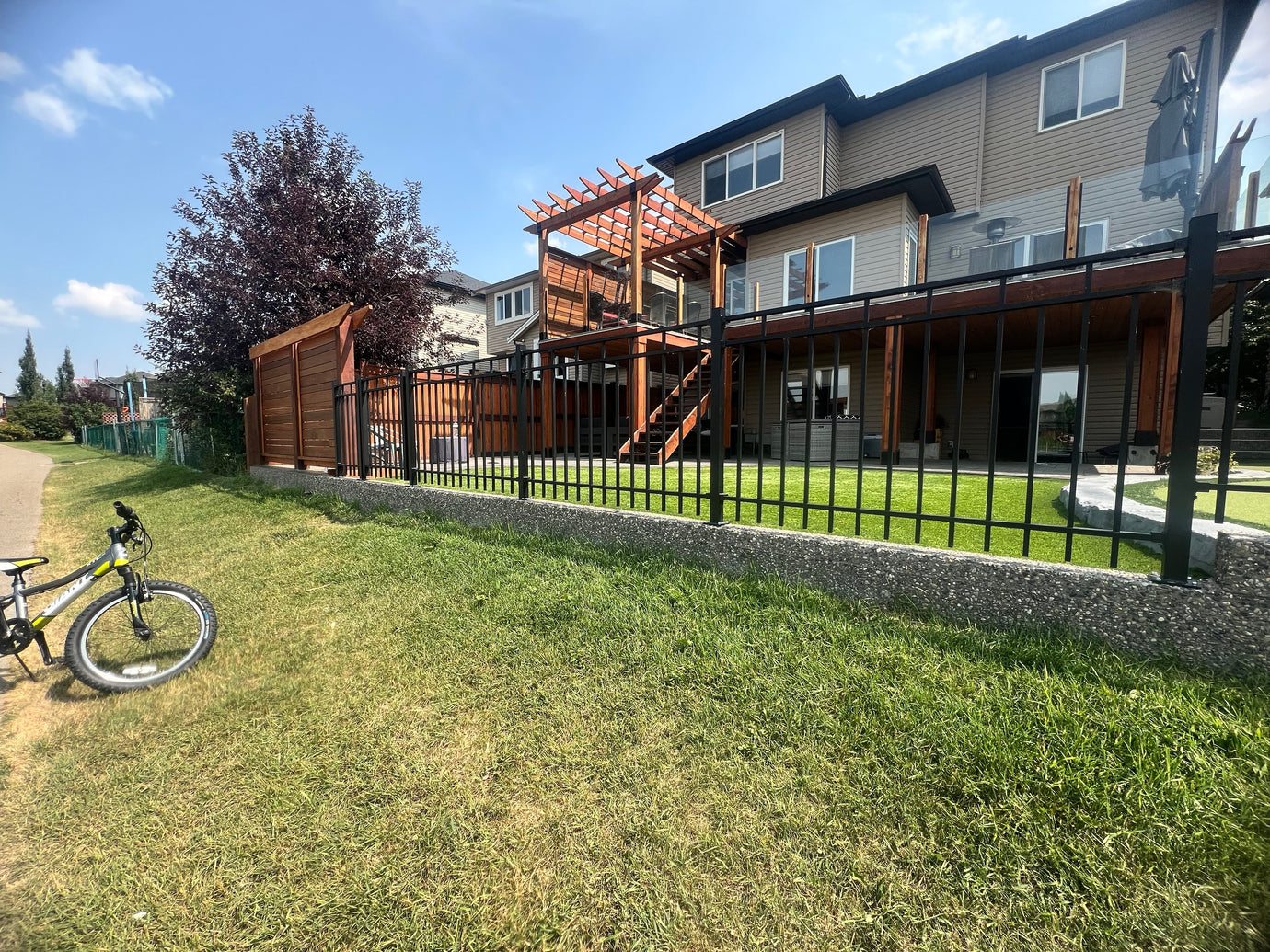 backyard of house showcasing gate and dark wooden deck representing residential landscape architecture