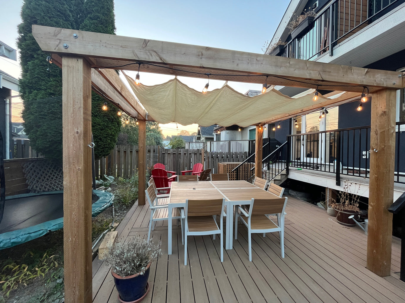 retractable shade sail pergola over a large patio set in a backyard with a deck and a trampoline