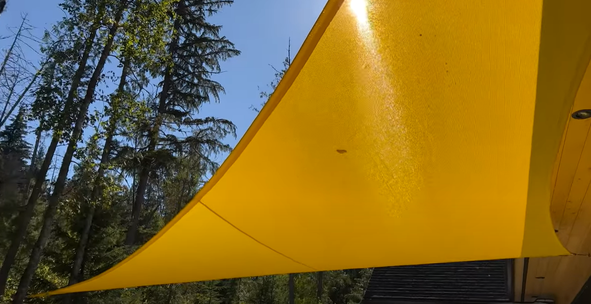 yellow shade sail attached to tree showcasing monofilament fabric