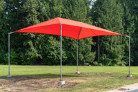 A bright red square canopy shade tent with a silver metal frame and concrete base pads, set up on a grassy lawn with a background of green trees.