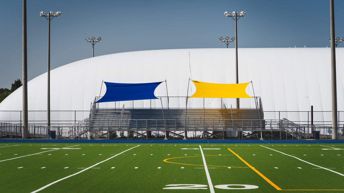 Football field with bleachers and two colorful flags on a clear day
